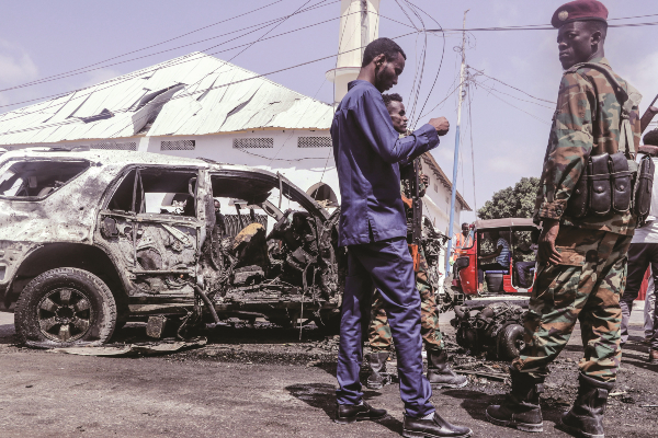 Officials gather beside debris at the site of a suicide car bombing attack near a security checkpoint in Mogadishu on February 13 2021